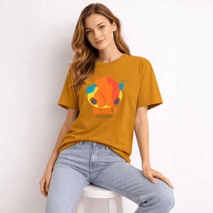 Woman wearing a mustard yellow t-shirt with a colorful bear graphic and text, sitting on a white stool against a light background.