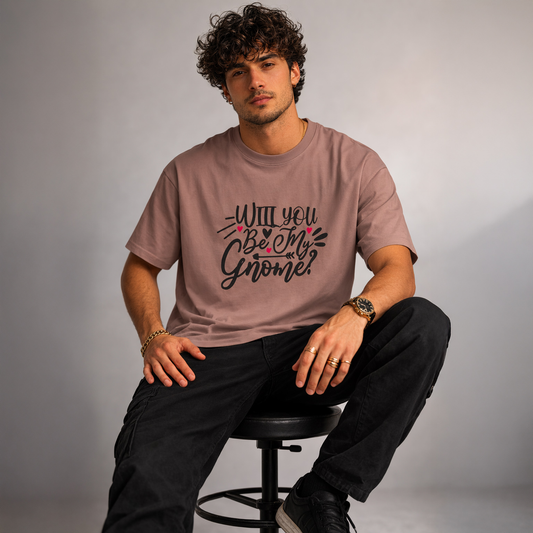 Man wearing a brown t-shirt with text, sitting on a stool against a plain background