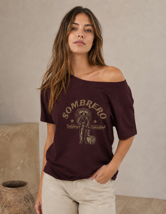 Woman wearing a maroon t-shirt with 'Sombrero' graphic design against a beige wall.
