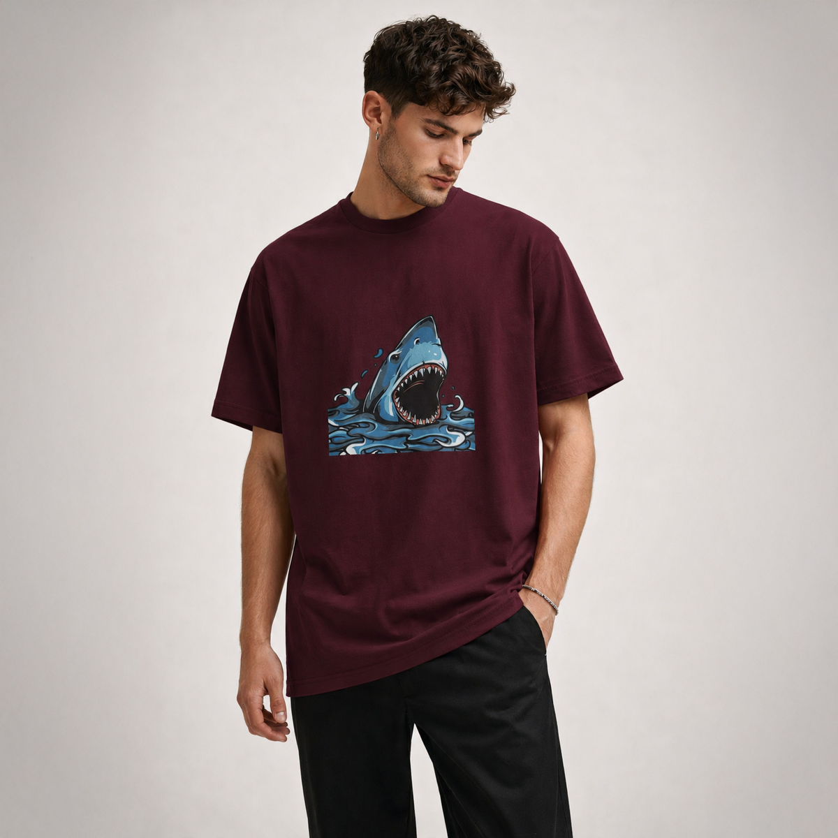 Man wearing a burgundy t-shirt with a shark graphic on a plain background