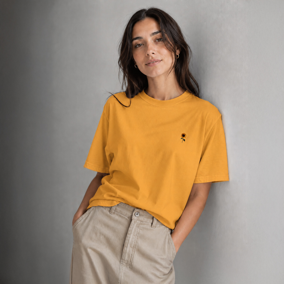 Woman wearing a mustard yellow t-shirt with a small black design against a gray background